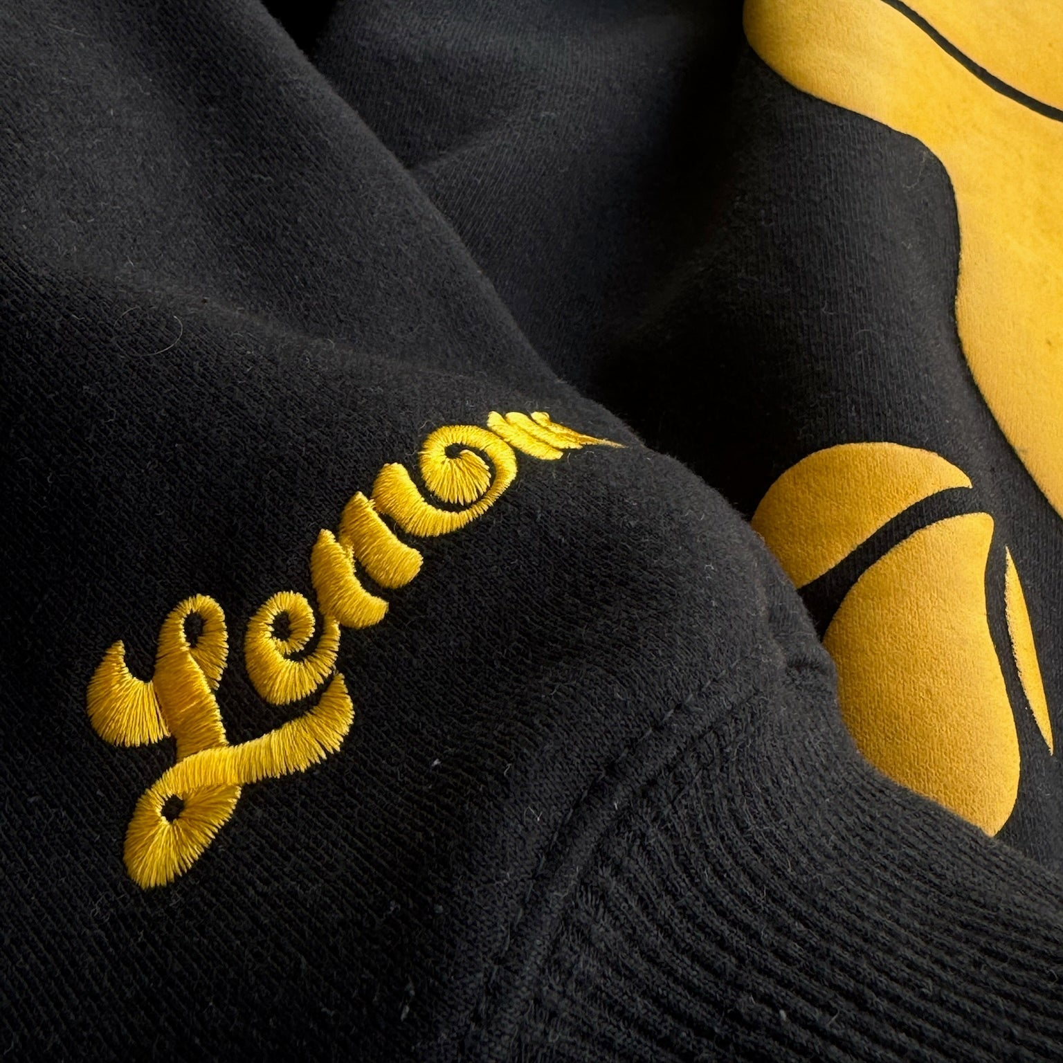 Black fabric with yellow embroidered text and a yellow graphic design.