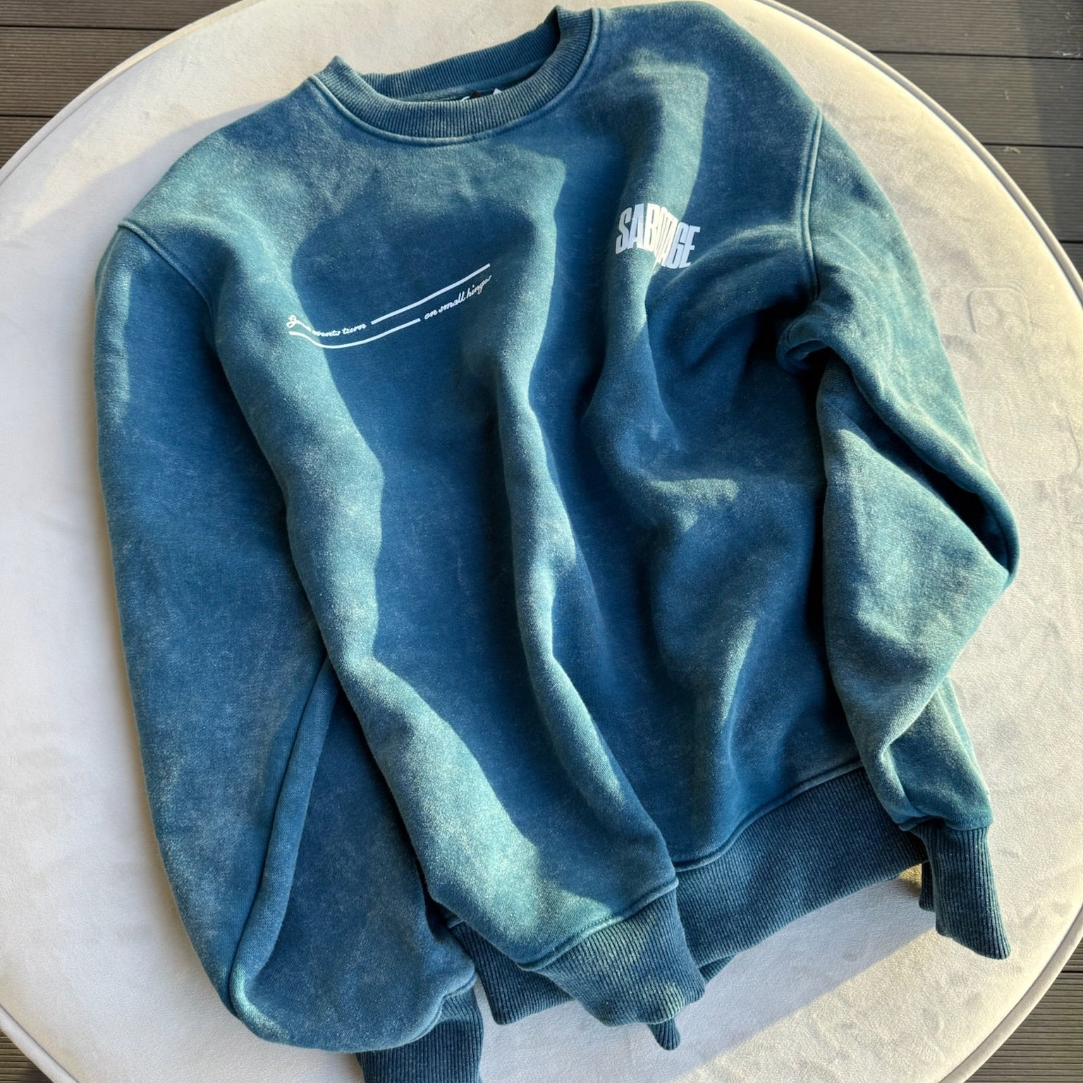 Blue sweatshirt with text on a white plate on a wooden surface