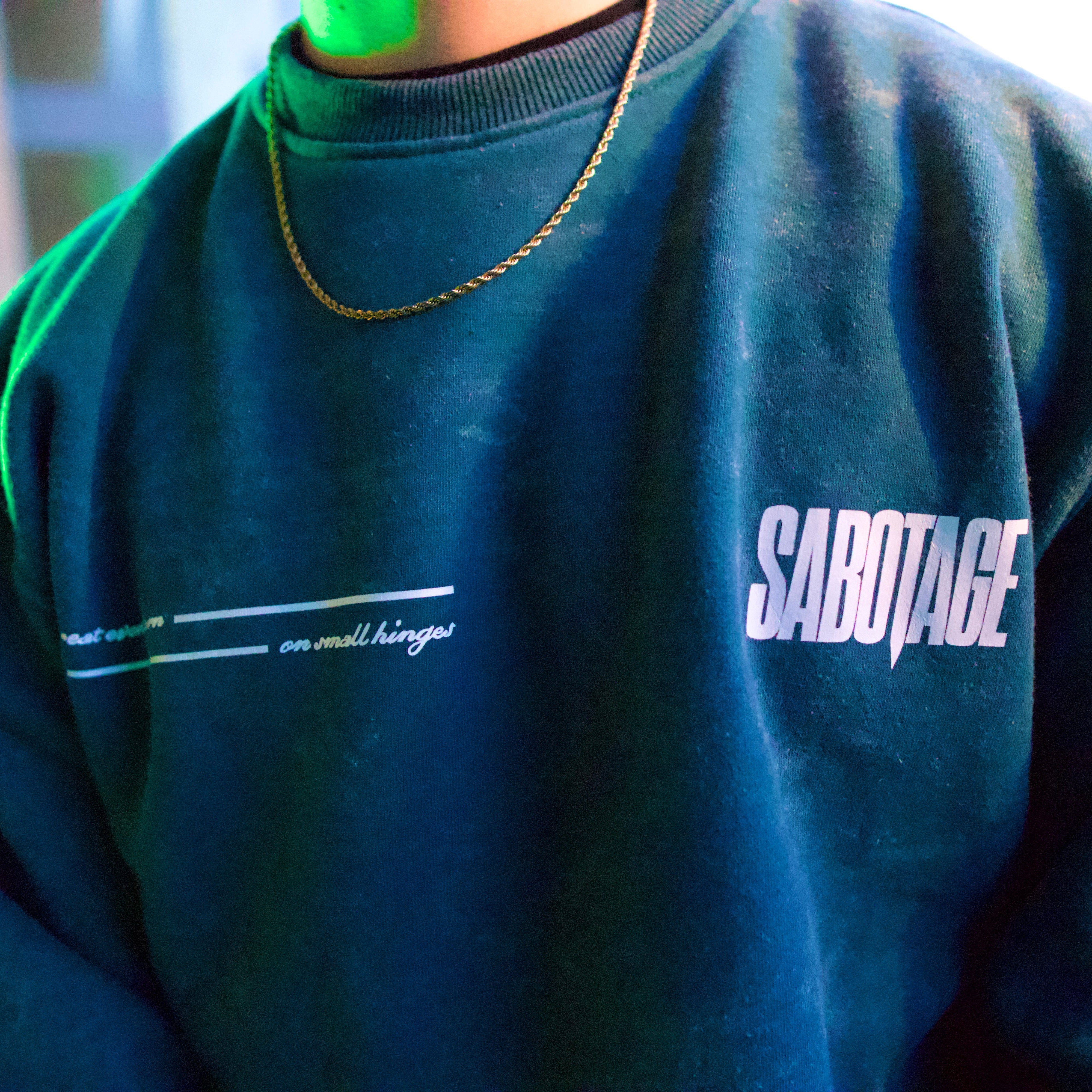 Person wearing a blue sweatshirt with 'SABOTAGE' printed on it, blurred background