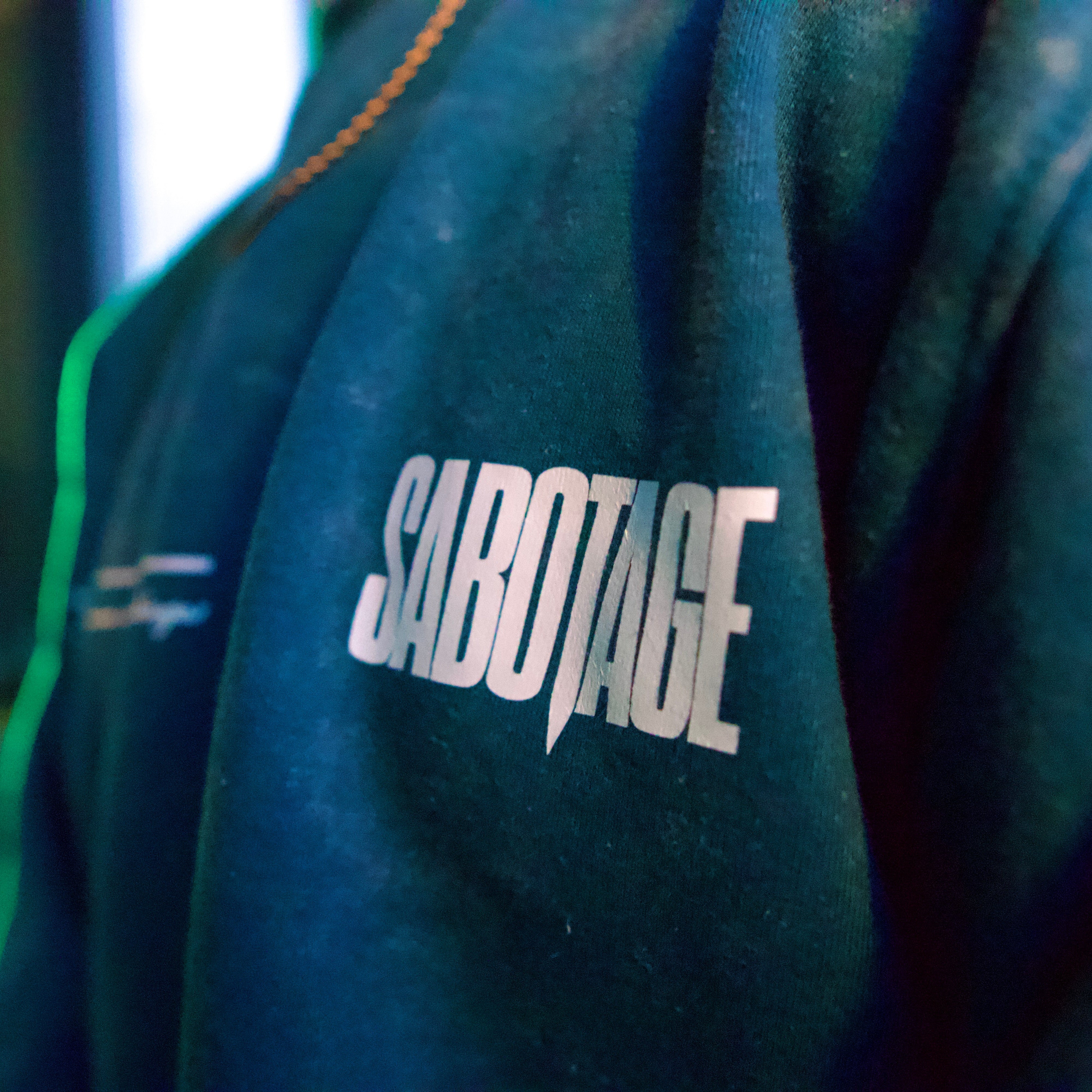 Teal sweatshirt with 'Sabotage' logo on a blurred background