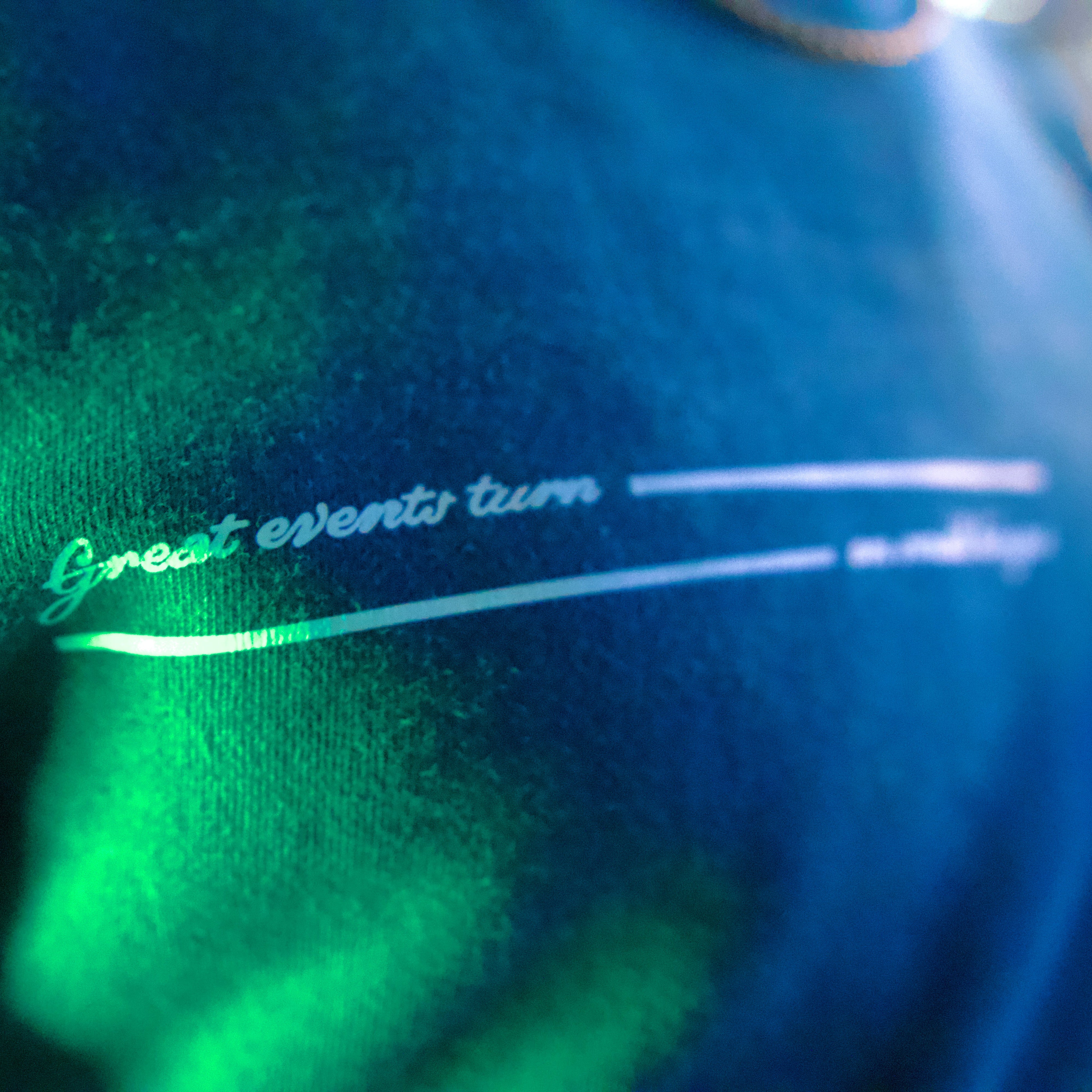 Teal sweatshirt with text 'Great events turn on small hinges' in a dark setting